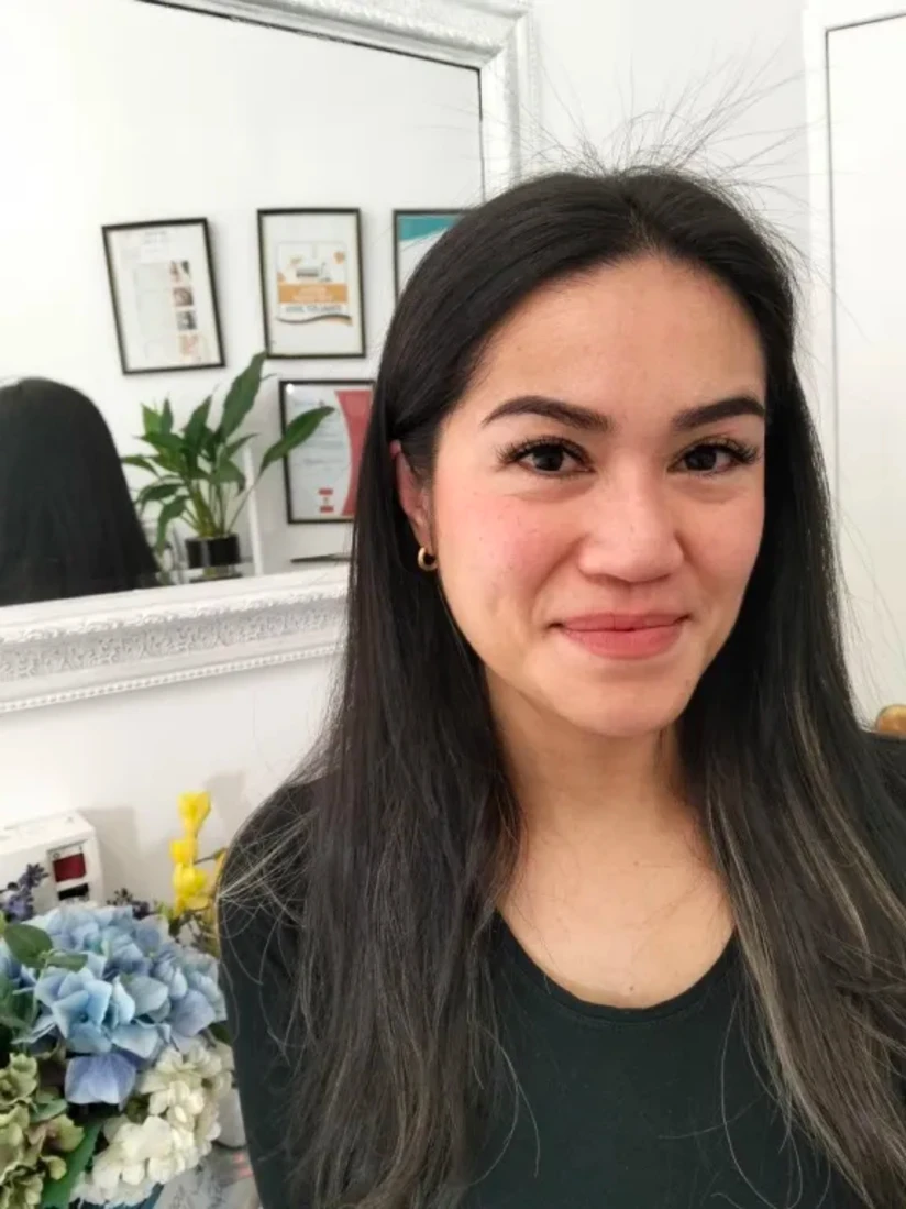 A client smiling after her appointment, wearing a gold hoop earring, her lash extensions dark against fair skin