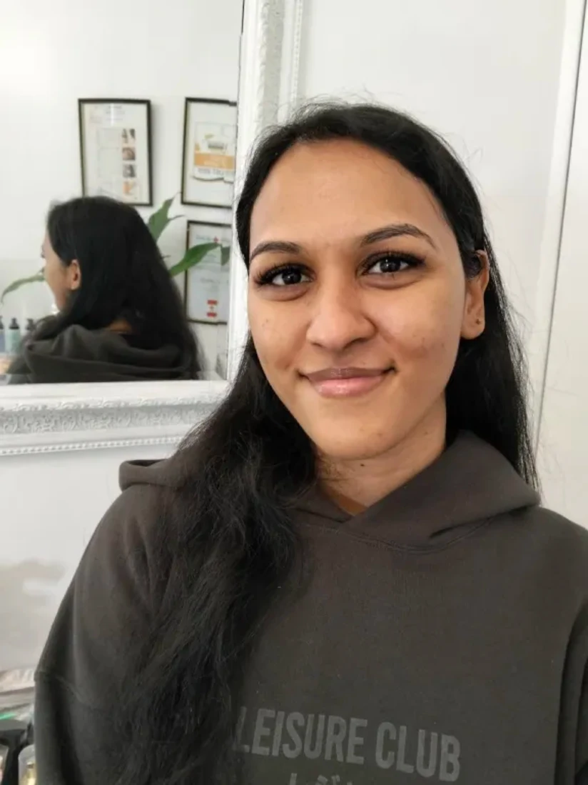 A client smiling with long dark hair over one shoulder, her lash extensions lifting the outer corner of the eye