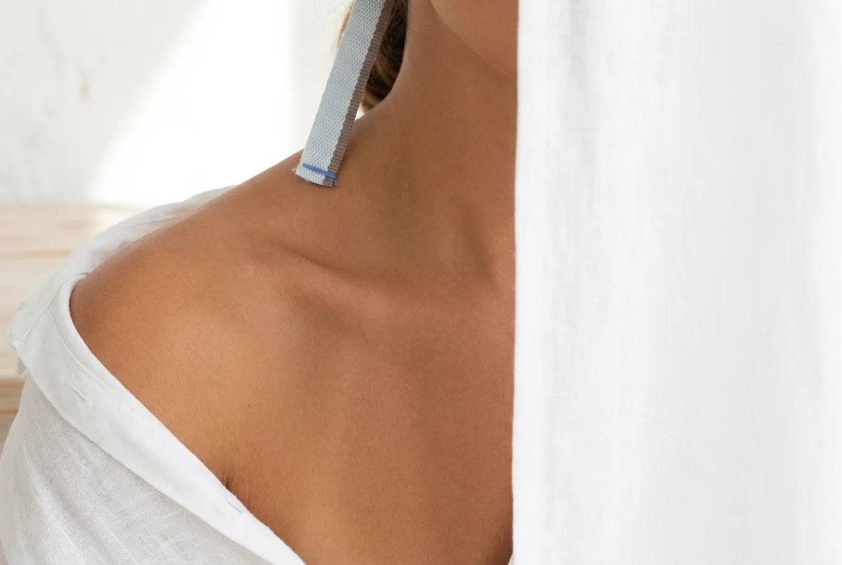 An evenly tanned shoulder and collarbone against white linen in daylight